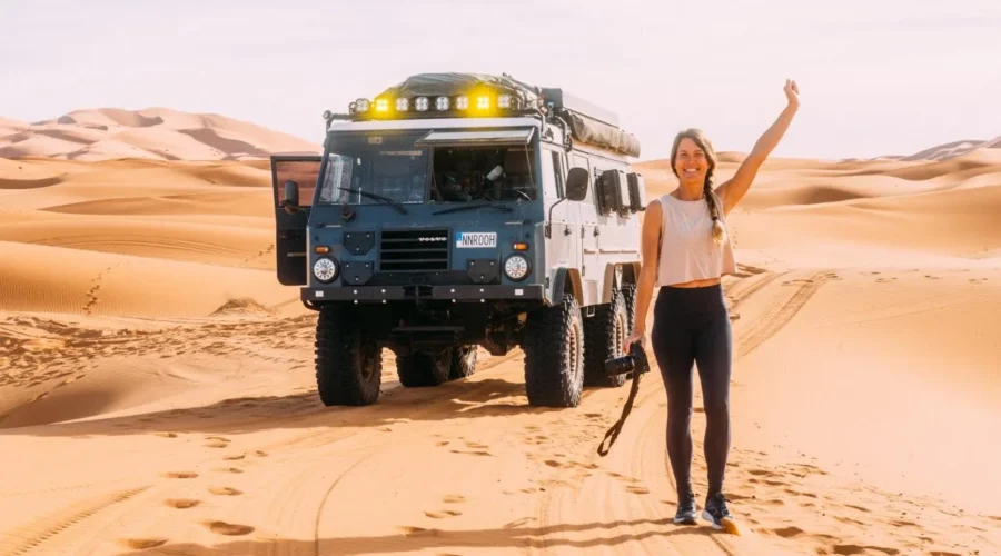 Traveler beside a 4x4 expedition truck in the Merzouga desert dunes, Morocco.